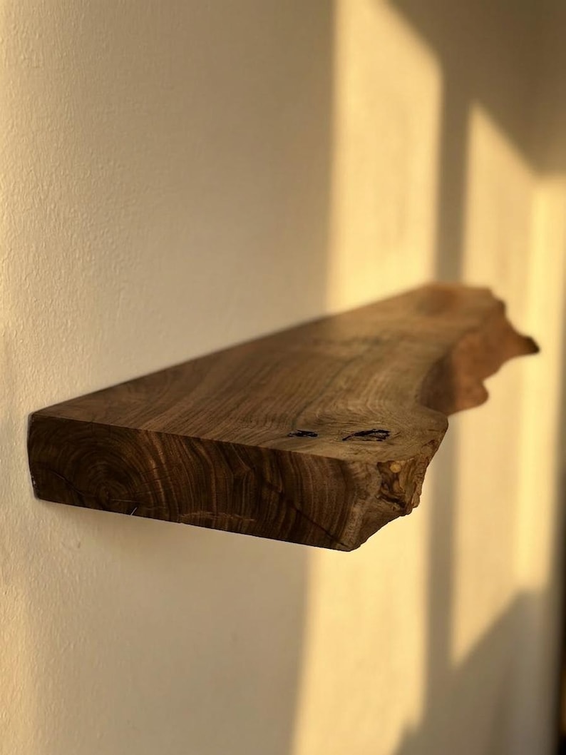 May include: A floating wooden shelf with a natural edge, mounted on a light-colored wall. The shelf is a rich brown color, showcasing the wood grain. The shelf is approximately 30 inches long.