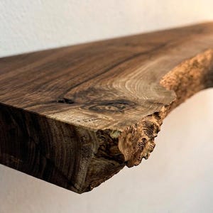 May include: A close-up of a rustic, wooden shelf with a natural edge. The shelf is a rich, dark brown color with visible wood grain and knots. The edge has a rough, textured appearance, showcasing the natural wood.