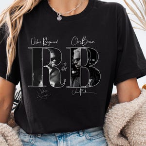 May include: Black t-shirt featuring a graphic design with the text "R&B" and the names "Usher Raymond" and "Chris Brown". The design includes black and white portraits of the artists and their signatures.