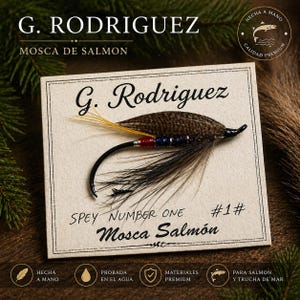 May include: A handcrafted salmon fly with a black, yellow, and brown feather design, mounted on a card. The card features the text "G. Rodriguez," "Spey Number One," and "Mosca Salmón." The fly is designed for salmon and sea trout.