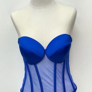 May include: A royal blue corset top with a sweetheart neckline and boning details. The bodice is made of a sheer mesh material with vertical boning. The top is displayed on a mannequin.