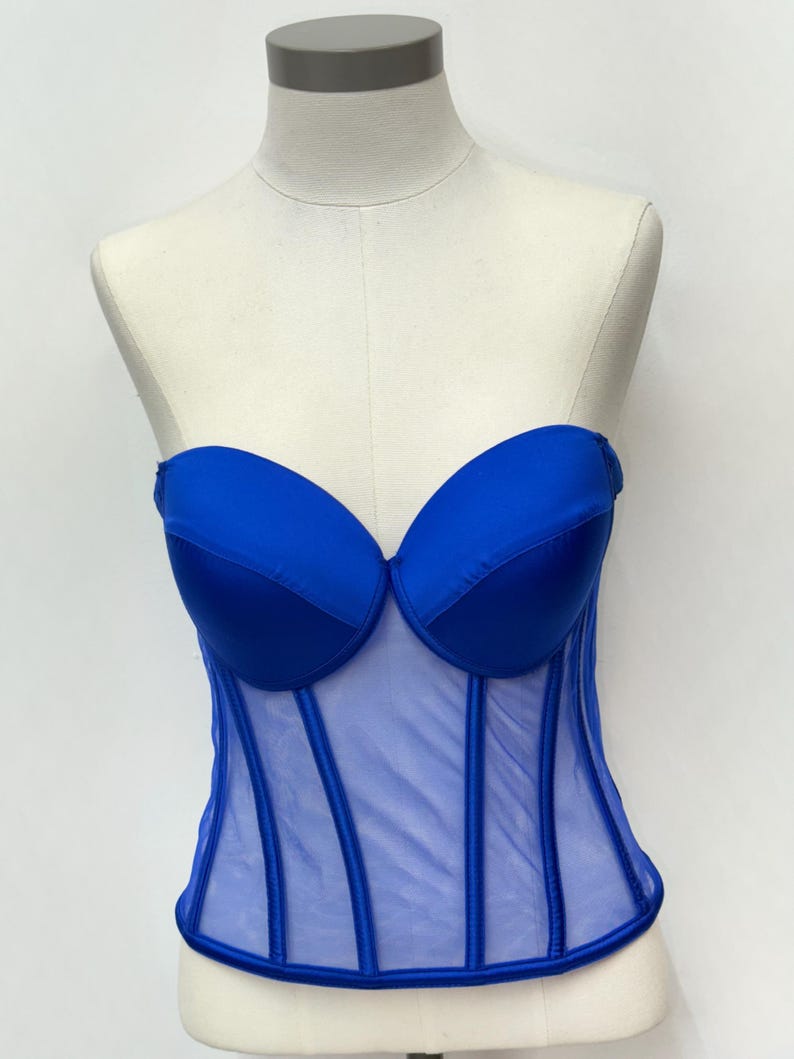 May include: A royal blue corset top with a sweetheart neckline and boning details. The bodice is made of a sheer mesh material with vertical boning. The top is displayed on a mannequin.