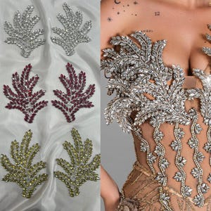 Puede incluir: Un surtido de adornos decorativos en forma de hoja en plata, burdeos y oro. Las hojas plateadas y doradas están adornadas con cristales brillantes. Las hojas burdeos también están adornadas con cristales. Las hojas se muestran sobre una tela blanca.