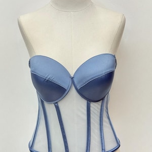 May include: A strapless, blue corset with a sheer, white mesh body. The bust is a solid, darker blue, and the boning is a lighter blue. The corset is displayed on a mannequin.