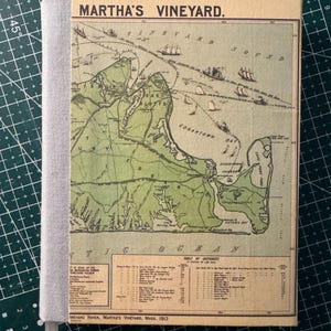May include: A vintage map of Martha's Vineyard, with the title at the top. The map is in shades of green and tan, with a gray fabric spine. The map includes the text "Vineyard Sound" and "Table of Distances".