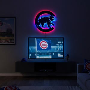 Puede incluir: Un letrero LED circular montado en la pared que presenta la silueta de un oso negro centrada dentro de una letra C grande. El letrero emite un brillo rojo vibrante detrás del marco circular y una luz azul brillante que delinea la figura del oso.