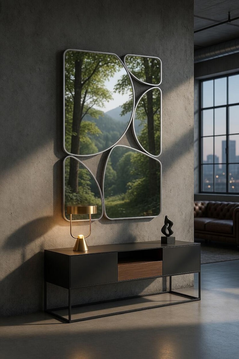 May include: A modern living room featuring a set of abstract-shaped mirrors with a forest view reflection. Below, a black console table with a gold lamp and a black sculpture. The room has a concrete wall and a large window.