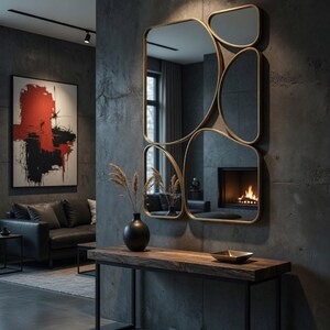 May include: A modern interior featuring a large, multi-paneled gold-framed mirror. Below the mirror is a dark wood console table with a black metal frame. A black vase with dried plants sits on the table. A painting with red and black brushstrokes hangs on the wall.