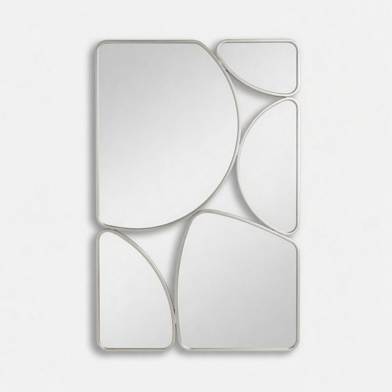 May include: A modern wall mirror with an abstract design. The mirror is composed of several irregularly shaped, rounded rectangles and semi-circles, all framed in a thin, silver-colored metal. The reflective surfaces are bright and clean, creating a contemporary aesthetic.