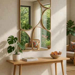 May include: A modern wall mirror with a gold frame, featuring an abstract design of connected rectangular and curved shapes. A wooden console table holds a potted plant, a book, and a bowl of dried fruit. The room has a neutral color palette.