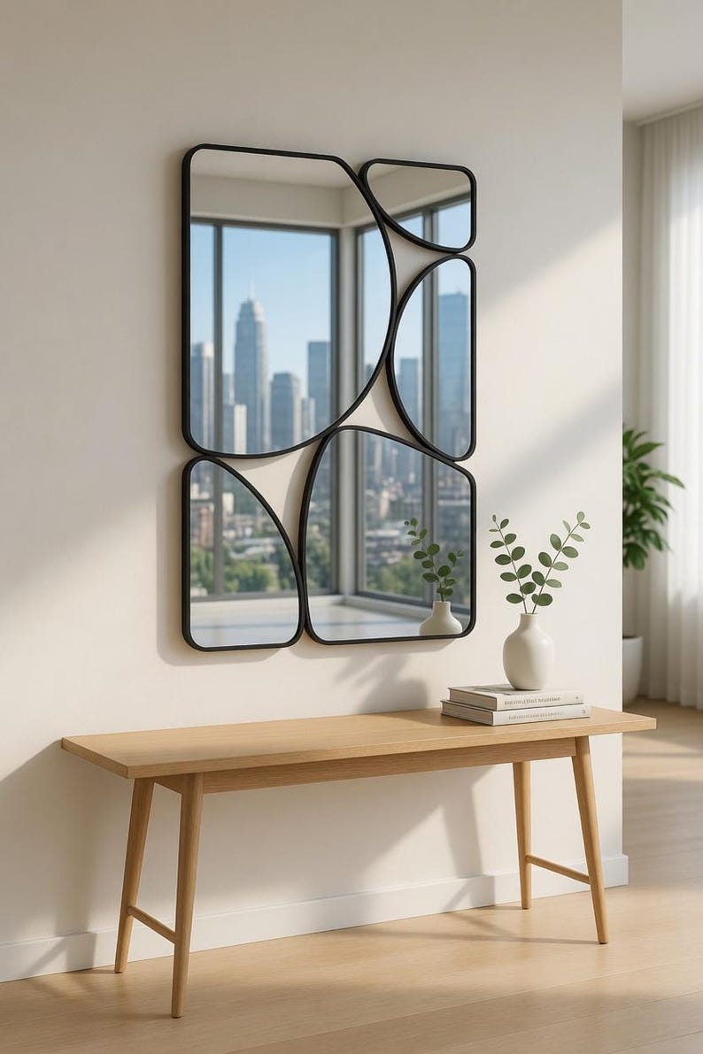 May include: A modern wall mirror with a unique design, featuring multiple irregularly shaped black-framed mirrors. The mirrors reflect a cityscape. Below, a light wood bench holds a white vase with greenery and books.