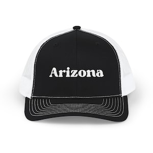 May include: Black and white trucker hat with the word "Arizona" in white block letters. The hat has a black front panel, a white mesh back, and a curved brim with white stitching. A classic and stylish accessory.
