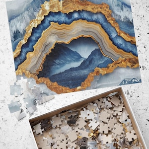 May include: A partially assembled jigsaw puzzle with a landscape design featuring blue and gold abstract elements. The puzzle's design includes a mountain scene. A box of puzzle pieces is nearby.