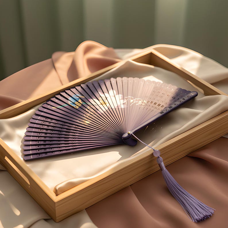 May include: A folding hand fan featuring a purple gradient background with a white floral design and a small blue bird illustration. The fan has a purple tassel attached to the handle, which is secured with a small metal pin at the pivot point.
