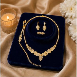 May include: A gold jewelry set consisting of a necklace, a bracelet, a pair of drop earrings, and a ring. Each piece features a textured gold finish with small, clear, sparkling stones arranged in a repeating wave and teardrop pattern.