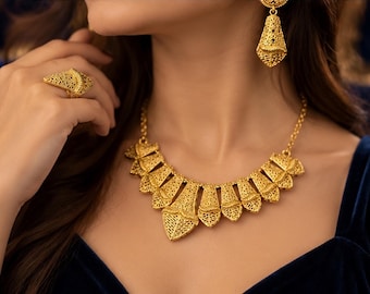 May include: A gold jewelry set consisting of a necklace, a ring, and a dangling earring. Each piece features an intricate, openwork filigree pattern with a textured, metallic finish. The necklace is composed of multiple fan-shaped segments.