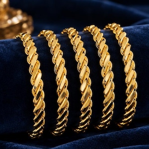 May include: Five gold-toned bracelets featuring a twisted, rope-like chain design. Each bracelet has a polished, reflective surface with a continuous interlocking pattern that creates a textured, cylindrical appearance throughout the length.
