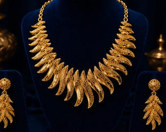 May include: A gold-toned necklace and matching earring set featuring a repeating leaf-like motif. The necklace consists of curved, filigree-style golden segments arranged in a fan shape, while the earrings mirror this design with a circular stud.