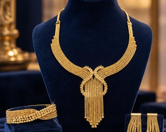 May include: A gold-toned jewelry set consisting of a multi-strand necklace with a central knotted tassel design, a matching multi-strand bracelet with beaded accents, and a pair of dangling multi-strand earrings with small gold beads.