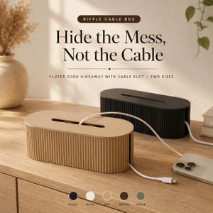 May include: Two oval-shaped cable management boxes with a fluted exterior design. One box is tan and the other is black. Each box features a rectangular slot on the top and a side opening for cords. Text reads: Riffle Cable Box, Hide the Mess, Not the Cable.