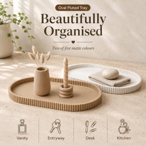 May include: Two oval fluted trays in beige and white matte finishes. The beige tray holds a fluted vase with dried stems and a twisted candle in a ring holder. The white tray holds a folded cloth and a round stone. Text reads Oval Fluted Tray.