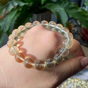 May include: A stretch bracelet composed of round, translucent, pale yellow beads. The beads exhibit a smooth, polished finish and are strung together on a clear elastic cord, creating a circular shape that reflects light across the surface.