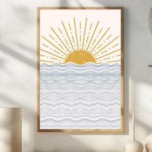 May include: A framed art print depicting a stylized sunrise over the ocean. The sun is golden yellow with radiating lines, and the ocean is shown with blue and white wave patterns. The artwork is in a wooden frame.