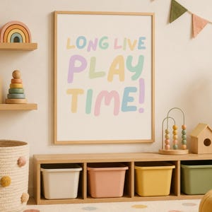 Könnte beinhalten: Ein rechteckiger Holzrahmen mit einem weißen Poster, das den Text LONG LIVE PLAY TIME! in pastellfarbenen Buchstaben zeigt. Der Rahmen hängt an einer Wand über einem niedrigen Holzregal mit vier farbigen Kunststoffbehältern.