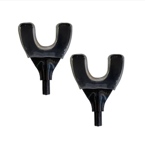 Pode incluir: Dois objetos pretos em forma de U com uma haste e uma base alargada. Os objetos são simétricos e parecem ser feitos de um material brilhante. O fundo é branco liso.