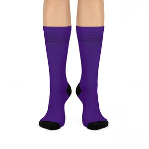 May include: A pair of purple socks with black heels and toes. The socks have text printed on them. The socks are displayed on a white background.
