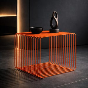 Peut inclure: Une table d'appoint en métal orange vif, de forme carrée. La table présente une structure en grille composée de barres verticales. Un bol noir et une sculpture abstraite sombre sont posés dessus.