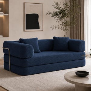May include: A modern, navy blue corduroy sofa with two matching throw pillows. The sofa has a low profile and a minimalist design, with a silver metal armrest. The sofa is placed on a light beige rug.