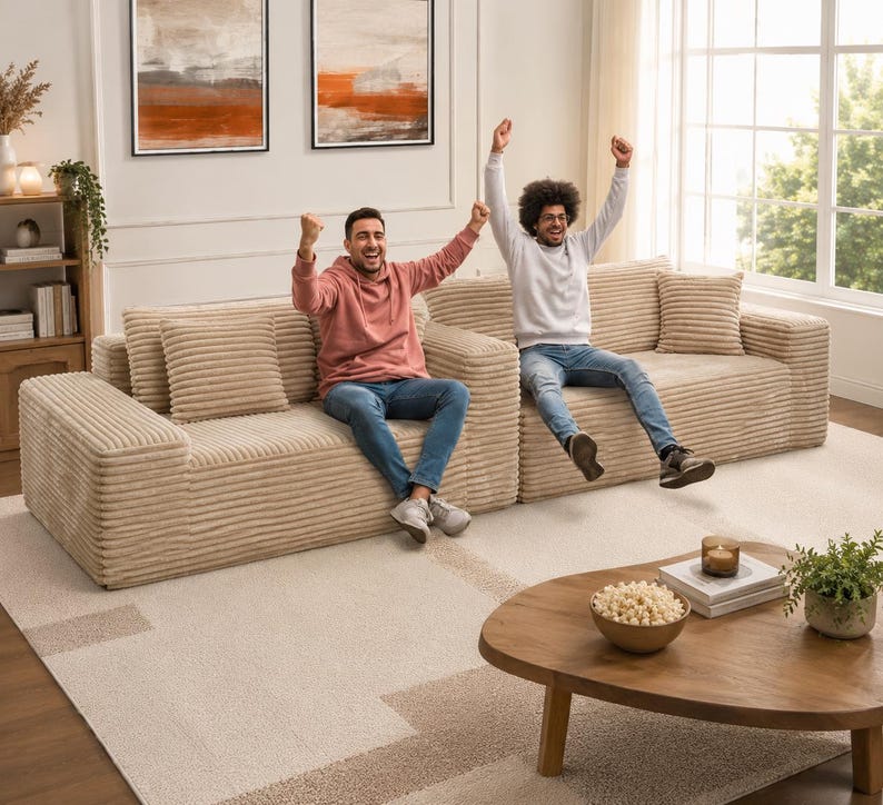 Puede incluir: Un sof&aacute; seccional de pana beige con cojines a juego. Dos personas est&aacute;n sentadas en el sof&aacute;, celebrando con los brazos levantados. Una mesa de centro de madera con un cuenco de palomitas y una planta est&aacute; frente al sof&aacute;.