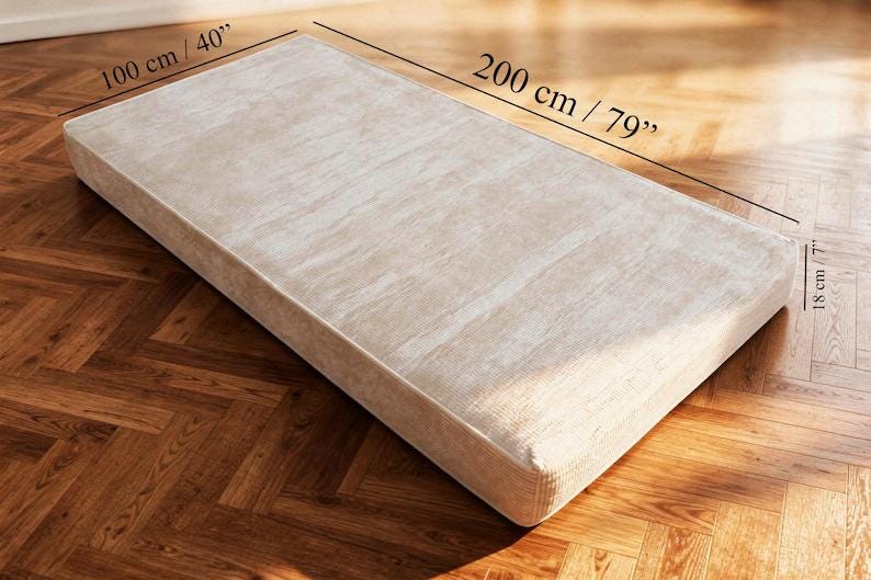 Puede incluir: Colch&oacute;n rectangular beige, de 200 cm de largo, 100 cm de ancho y 18 cm de grosor. El colch&oacute;n tiene una superficie texturizada y est&aacute; colocado sobre un suelo de madera.