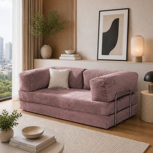 Puede incluir: Un sof&aacute; de pana rosa empolvado con un coj&iacute;n a juego y detalles cromados. El sof&aacute; es el punto focal de un sal&oacute;n moderno, complementado con una alfombra neutra, obras de arte y una mesa de centro redonda.