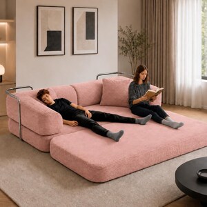 Puede incluir: Un gran sof&aacute; modular rosa de pana con una extensi&oacute;n de chaise longue. El sof&aacute; tiene un dise&ntilde;o moderno con reposabrazos de metal. Una persona est&aacute; acostada en la chaise longue y otra est&aacute; leyendo un libro. La habitaci&oacute;n tiene una paleta de colores neutros.