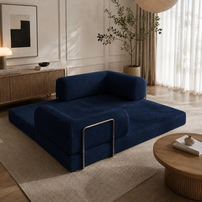 May include: A modular navy blue sofa with a low profile and rounded armrests. The sofa is composed of several sections, including a flat base and cushioned backrests. A silver metal frame is visible on one section. The sofa is placed on a neutral-toned rug.