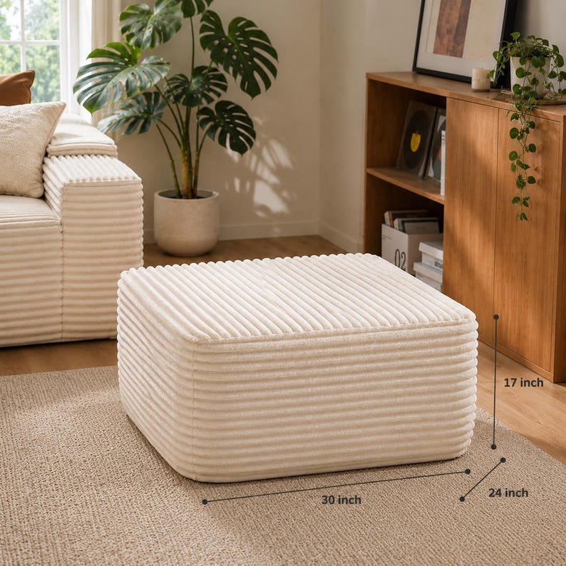 Puede incluir: Otomana de pana color crema, rectangular, con dimensiones de 76 cm de largo, 61 cm de ancho y 43 cm de alto. La otomana est&aacute; colocada sobre una alfombra de tono neutro. Parte de un juego de muebles de sal&oacute;n.