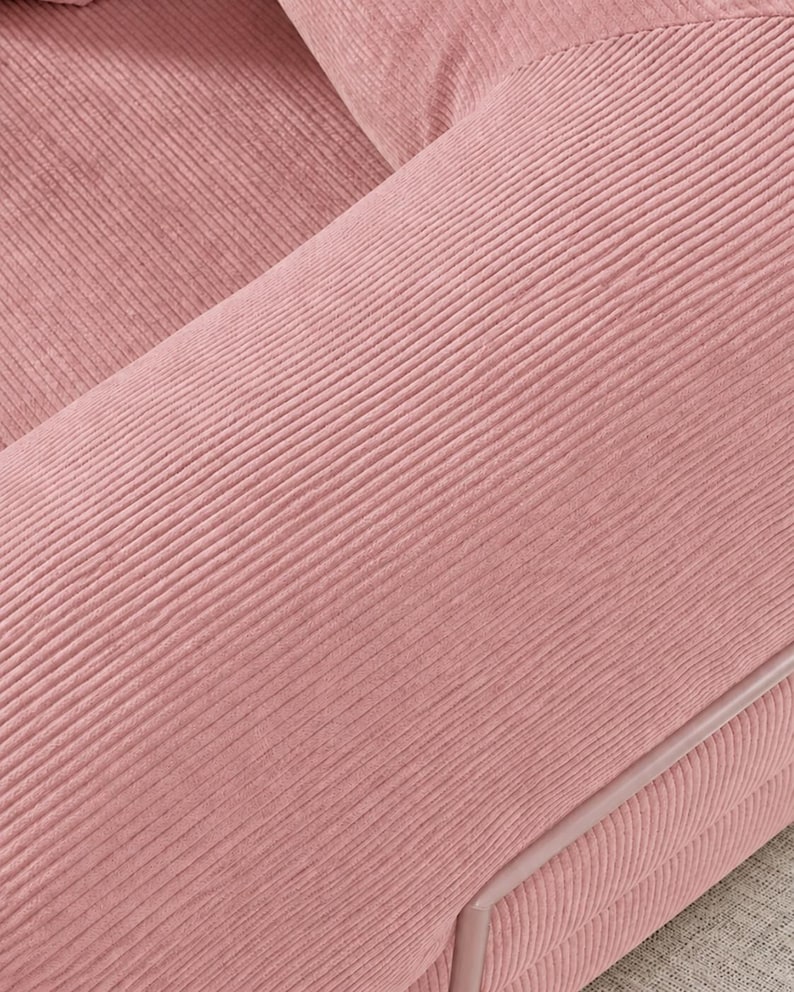 Puede incluir: Primer plano de una secci&oacute;n de un sof&aacute; de pana rosa. La tela tiene una textura acanalada, con las crestas que corren diagonalmente a trav&eacute;s del marco. Los bordes est&aacute;n ribeteados con una tuber&iacute;a rosa m&aacute;s clara.