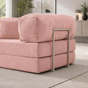 Puede incluir: Sof&aacute; modular de pana rosa con un dise&ntilde;o minimalista. El sof&aacute; presenta una construcci&oacute;n apilable en forma de bloques con un marco de metal. La tela de pana tiene una textura acanalada. El sof&aacute; est&aacute; sobre una alfombra de color neutro.