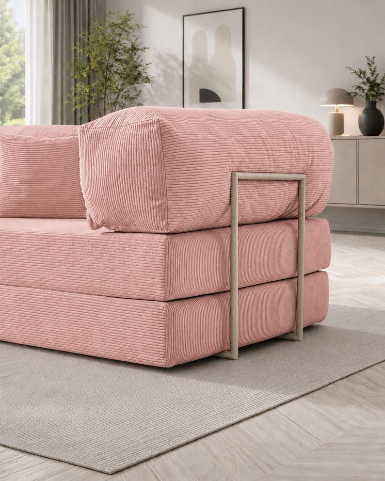 Puede incluir: Sof&aacute; modular de pana rosa con un dise&ntilde;o minimalista. El sof&aacute; presenta una construcci&oacute;n apilable en forma de bloques con un marco de metal. La tela de pana tiene una textura acanalada. El sof&aacute; est&aacute; sobre una alfombra de color neutro.