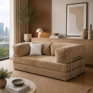 Puede incluir: Sal&oacute;n moderno con un sof&aacute; de pana beige. El sof&aacute; tiene un perfil bajo y detalles met&aacute;licos. Un coj&iacute;n blanco descansa sobre el sof&aacute;. La habitaci&oacute;n incluye una mesa de centro redonda, una alfombra y un mueble de madera. El conjunto es de tonos neutros.