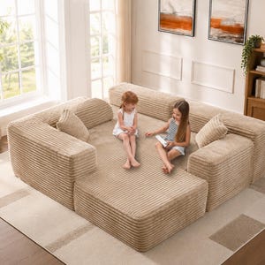 May include: A modular, beige corduroy sectional sofa with multiple pieces, including corner sections, a footstool, and throw pillows. The sofa is arranged on a neutral-toned rug in a living room setting. Two children are sitting on the sofa.