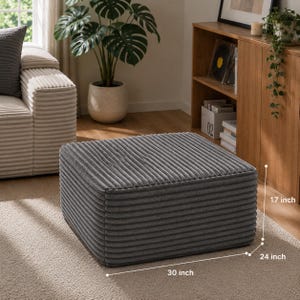 Puede incluir: Un otom&aacute;n de pana gris, de 76 cm de largo, 61 cm de ancho y 43 cm de alto. El reposapi&eacute;s rectangular est&aacute; sobre una alfombra beige. Un sof&aacute; y un mueble de madera est&aacute;n en el fondo, con una gran planta en maceta.