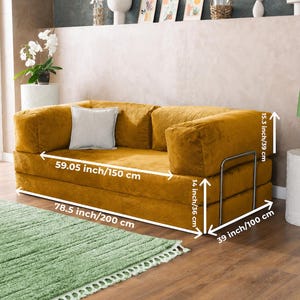 Puede incluir: Sof&aacute; de pana amarillo mostaza con un coj&iacute;n gris claro. El sof&aacute; mide 200 cm de largo, 150 cm de ancho y 100 cm de profundidad. Tiene una estructura met&aacute;lica y mide 39 cm de alto. Los reposabrazos miden 36 cm de alto.