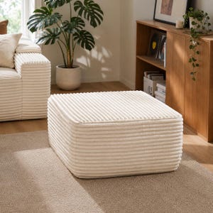 Puede incluir: Un otom&aacute;n de pana color crema, de forma cuadrada. Presenta una textura acanalada y est&aacute; colocado sobre una alfombra de tonos neutros. El dise&ntilde;o es simple y moderno, adecuado para la decoraci&oacute;n del sal&oacute;n. Dimensiones: aprox. 70 cm x 70 cm.
