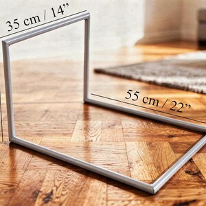 Puede incluir: Un marco de metal plateado, de 35 cm de ancho, 45 cm de alto y 55 cm de largo, est&aacute; sobre un suelo de madera. El marco tiene una forma geom&eacute;trica simple, posiblemente para exhibici&oacute;n o decoraci&oacute;n.