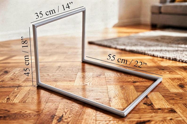 Puede incluir: Un marco de metal plateado, de 35 cm de ancho, 45 cm de alto y 55 cm de largo, est&aacute; sobre un suelo de madera. El marco tiene una forma geom&eacute;trica simple, posiblemente para exhibici&oacute;n o decoraci&oacute;n.