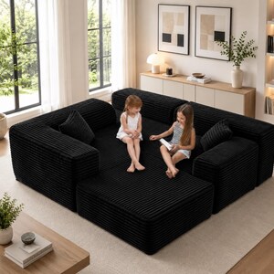Puede incluir: Un gran sof&aacute; modular de pana negro con m&uacute;ltiples secciones y cojines. El sof&aacute; est&aacute; dispuesto en forma de L y se coloca sobre una alfombra de color claro. Dos ni&ntilde;os peque&ntilde;os est&aacute;n sentados en el sof&aacute;.