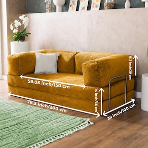 Puede incluir: Sof&aacute; de pana amarillo mostaza con un coj&iacute;n gris claro. El sof&aacute; mide 200 cm de largo, 150 cm de ancho y 100 cm de profundidad. Tiene una estructura met&aacute;lica y mide 39 cm de alto. Un mueble elegante.